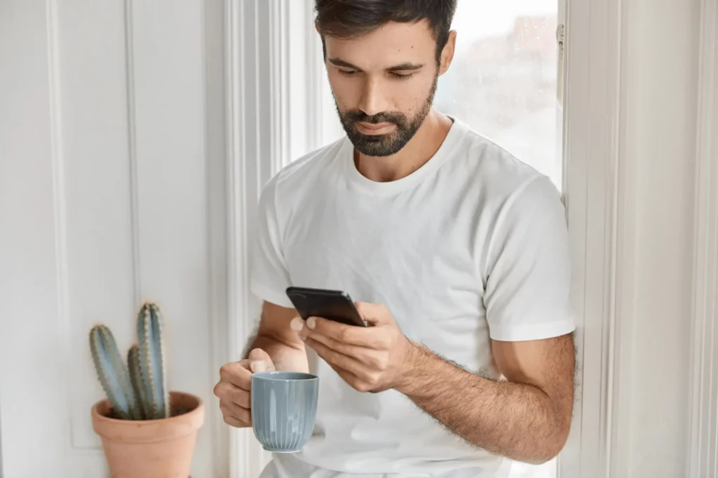 man using phone and holding tea mug